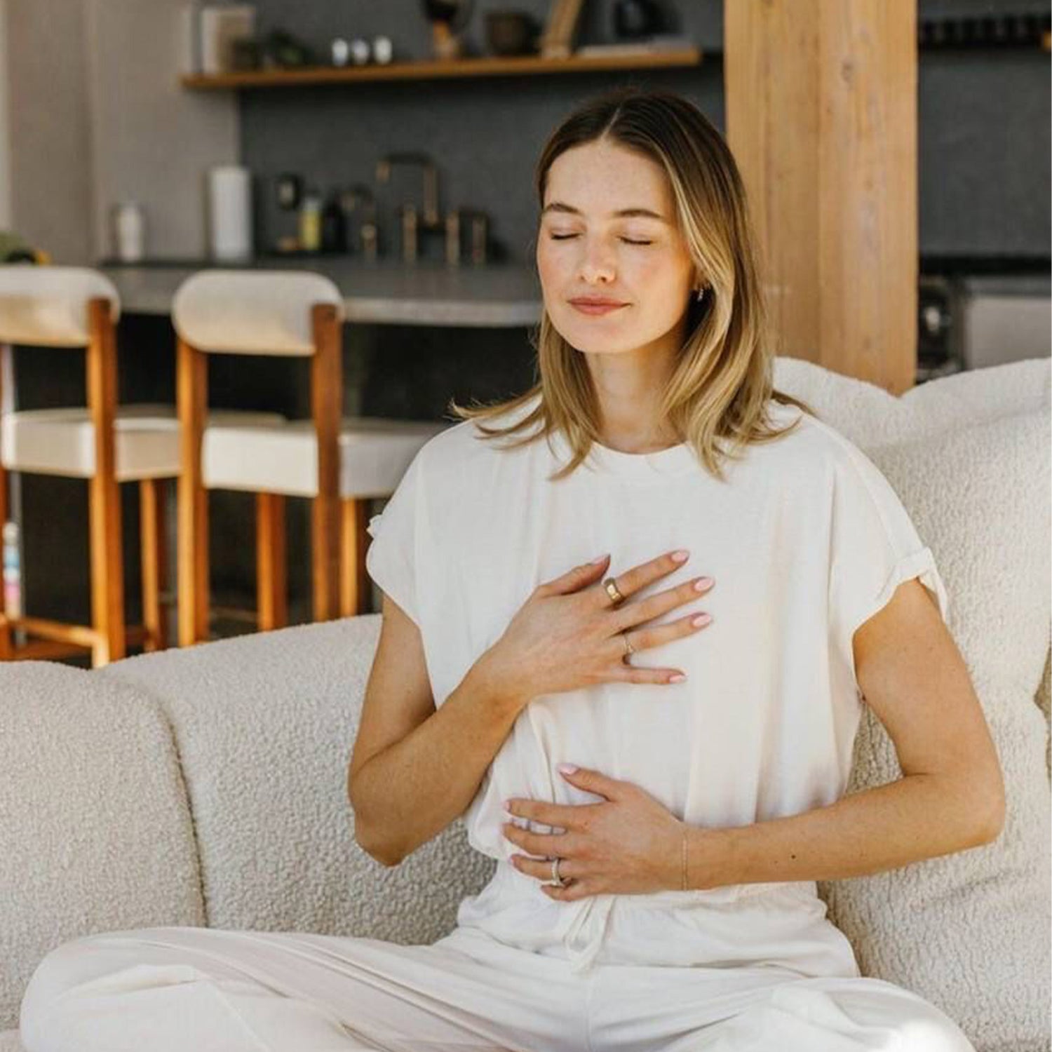 Woman sitting on a couch in a cozy living room, wearing a white outfit.